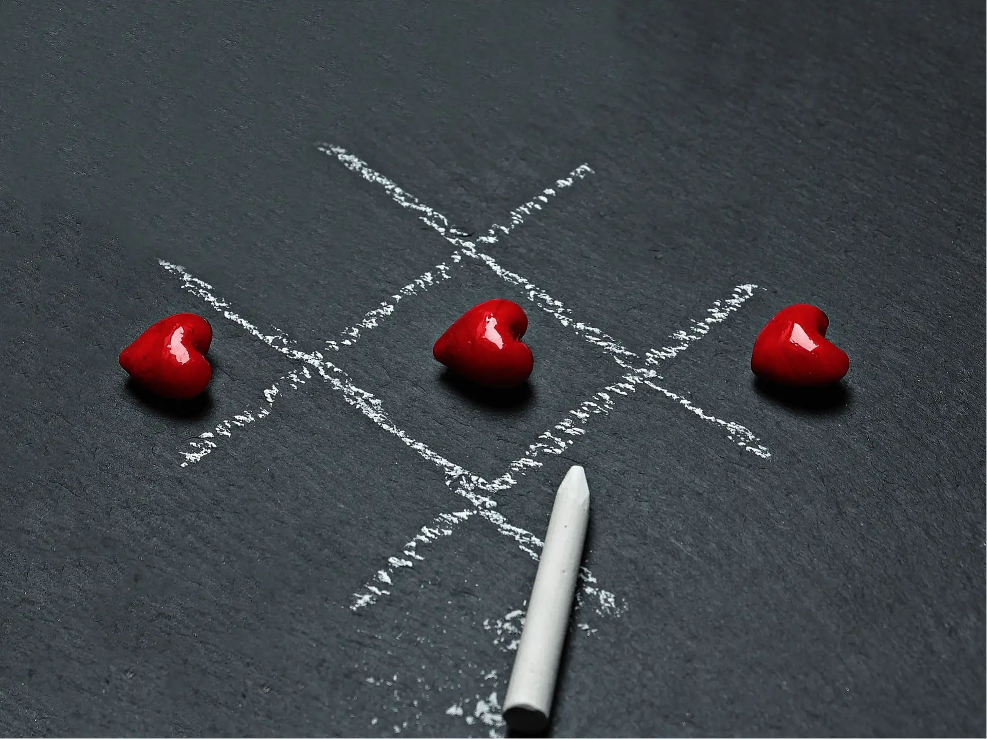 Tic-tac-toe game with red heart pieces on a chalkboard surface.